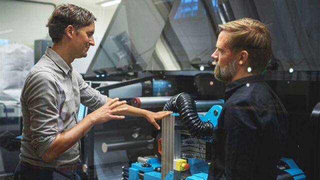 Two people in front of a roll-to-roll machine