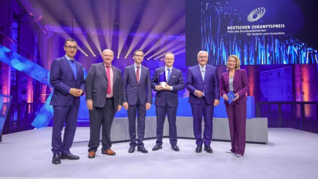 The winners of the Deutscher Zukunftspreises 2024, Dr. Norwin von Mal (center), Stefan Grötsch (third from right) and Dr. Hermann Oppermann (second from left) with Federal President Frank-Walter Steinmeier (second from right), Federal Minister for Education and Research Cem Özdemir (left) and moderator Yve Fehring (right)