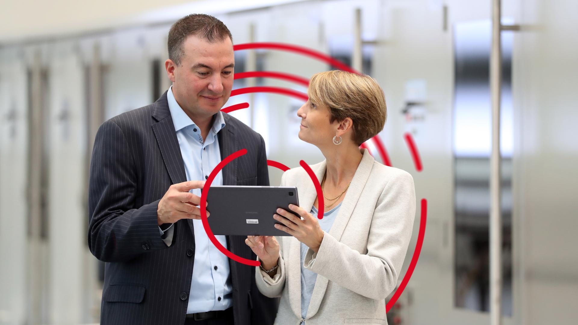 A man and a woman holding a tablet in front of a BOBST machine